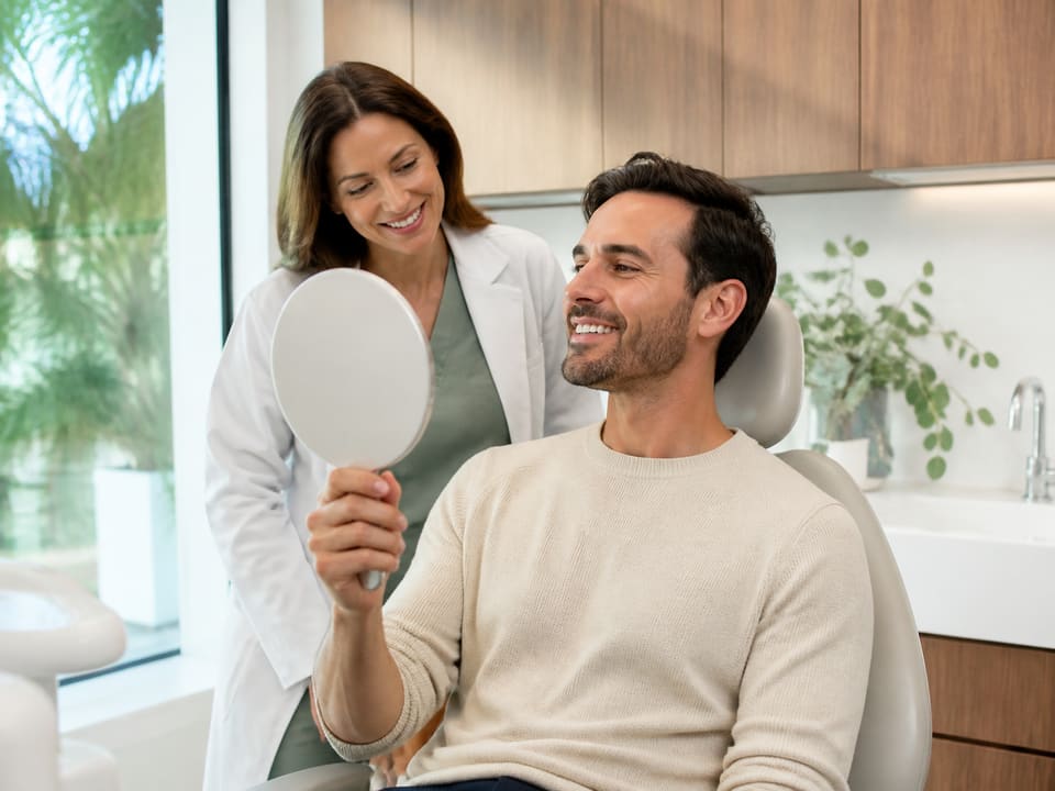 A woman smiling while looking at a hand mirror